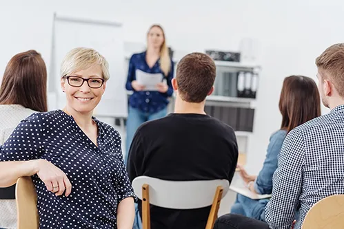 Lächelnde Mitarbeiterin in einer Teambesprechung mit Kolleginnen und Kollegen
